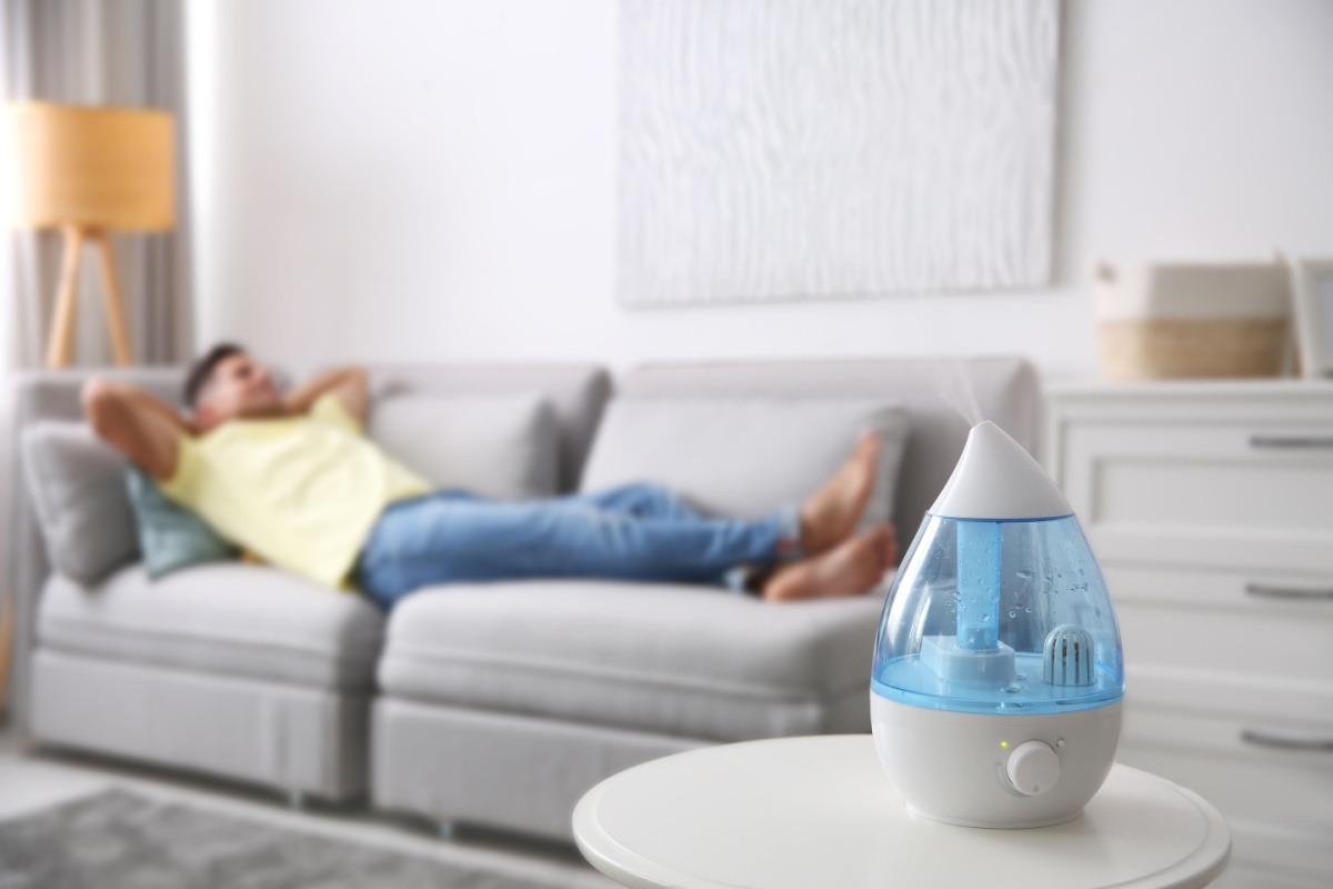 A man stretched out on the couch with a humidifier running in the foreground