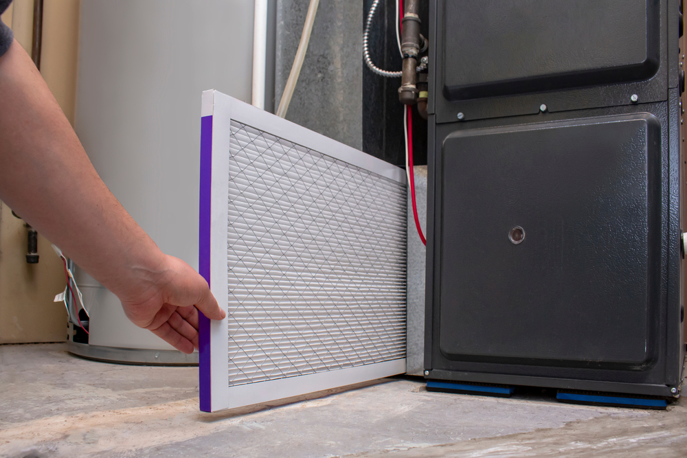 A man's hand holding a clean air filter as he is getting ready to install it in a furnace